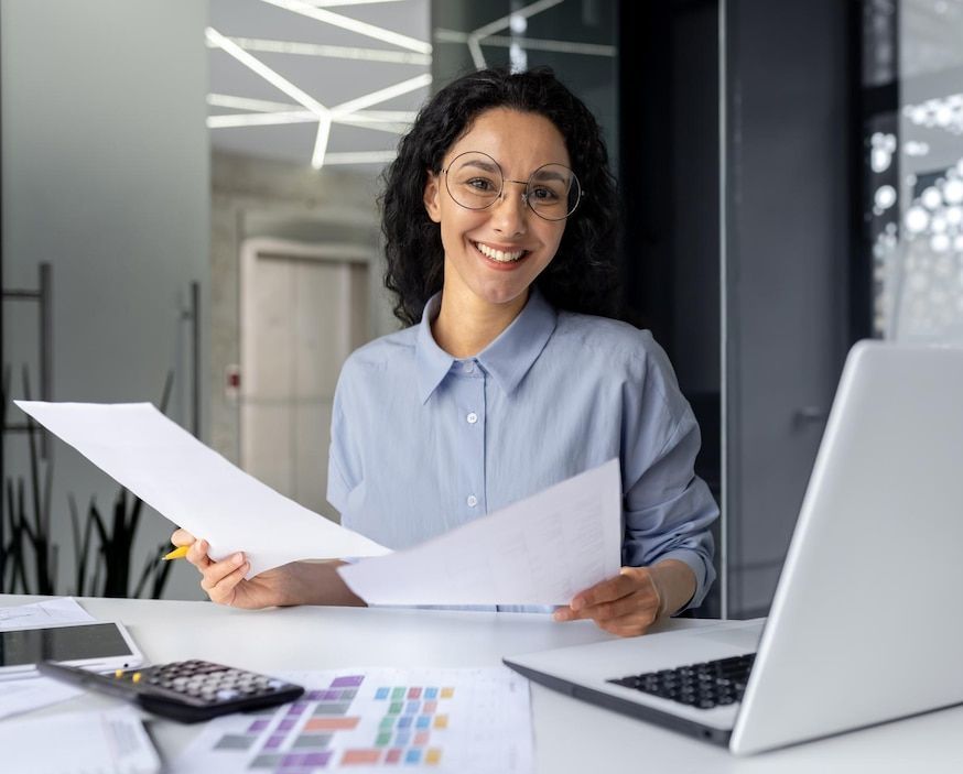 A woman is wearing a headset and smiling while sitting at a desk.