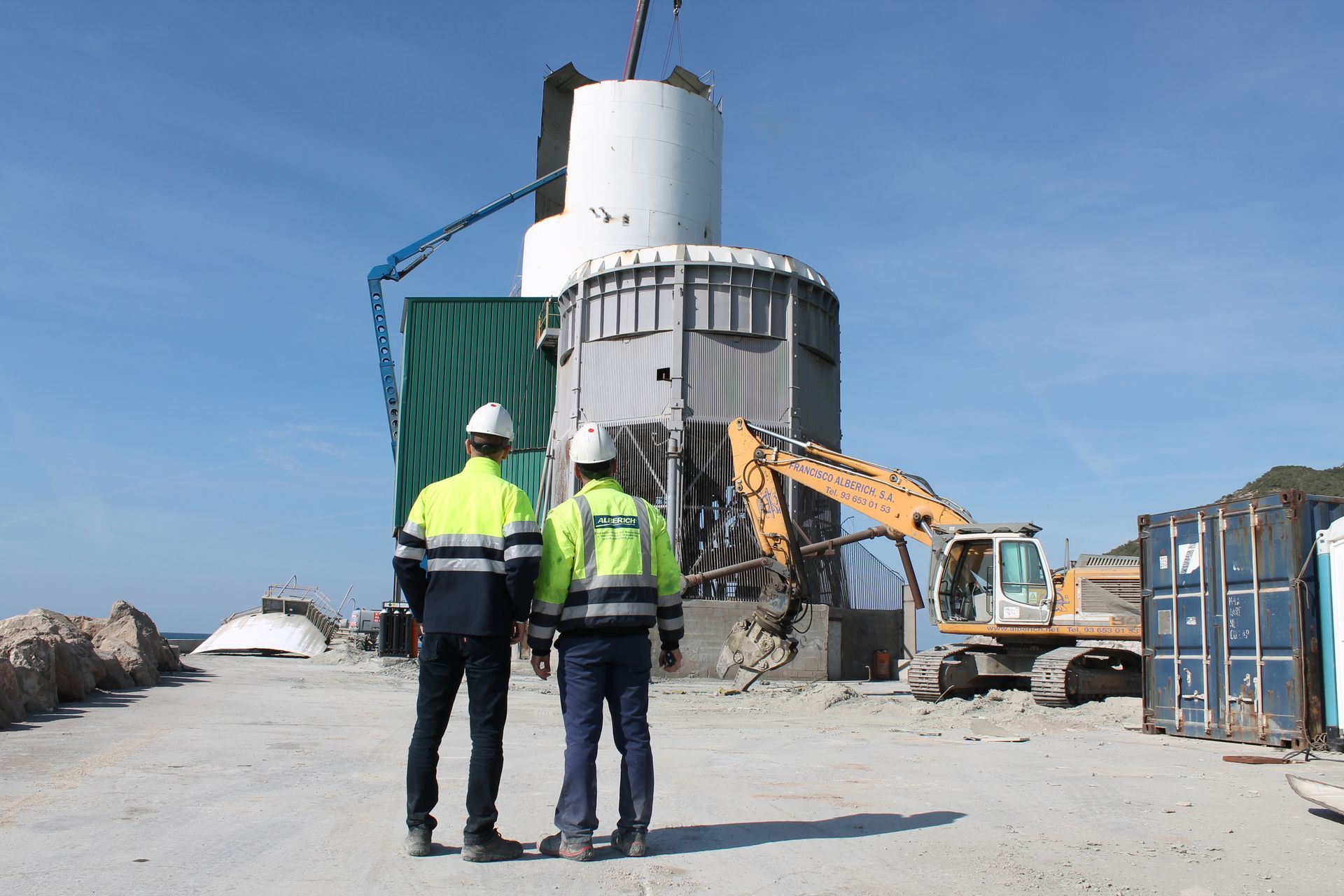 Two men in hard hats are standing in front of a large building.