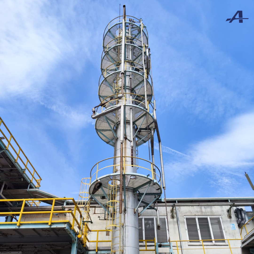 Tall industrial tower with spiral platforms against a blue sky, part of a factory setting.