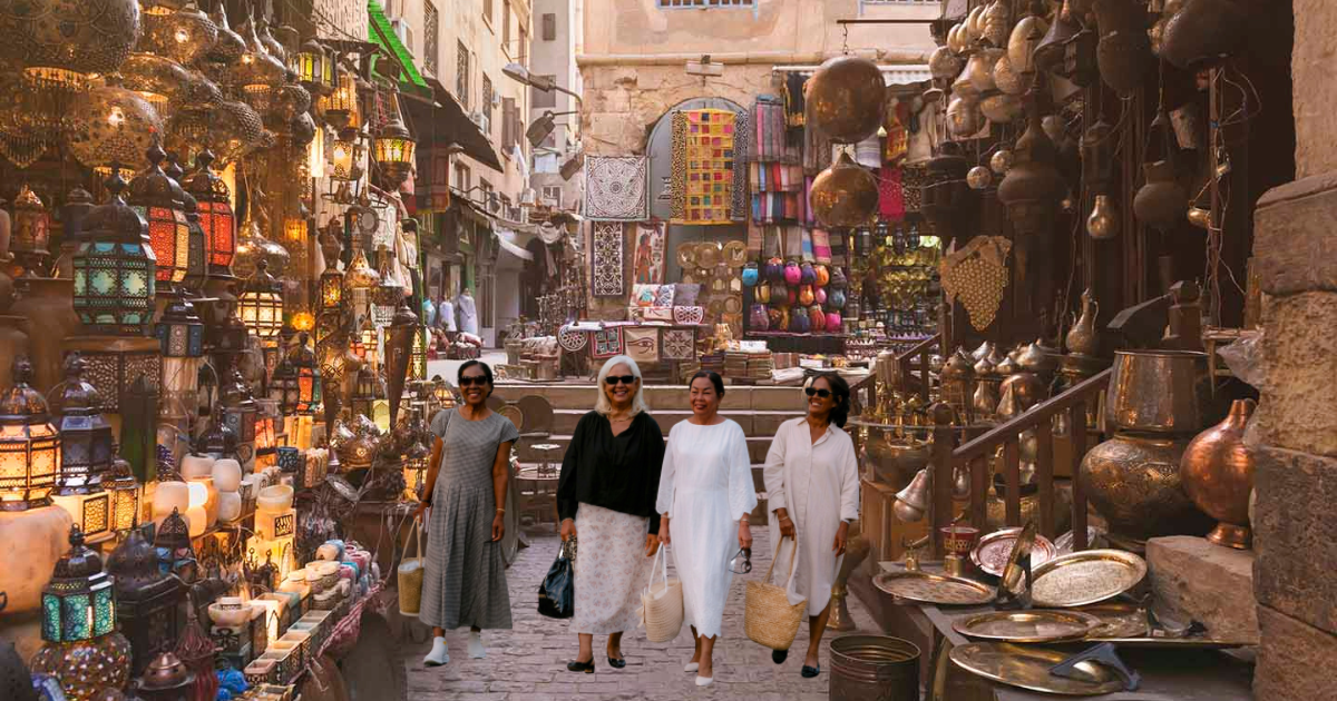 People walking through a narrow, lantern-filled market alley lined with hanging goods and pottery