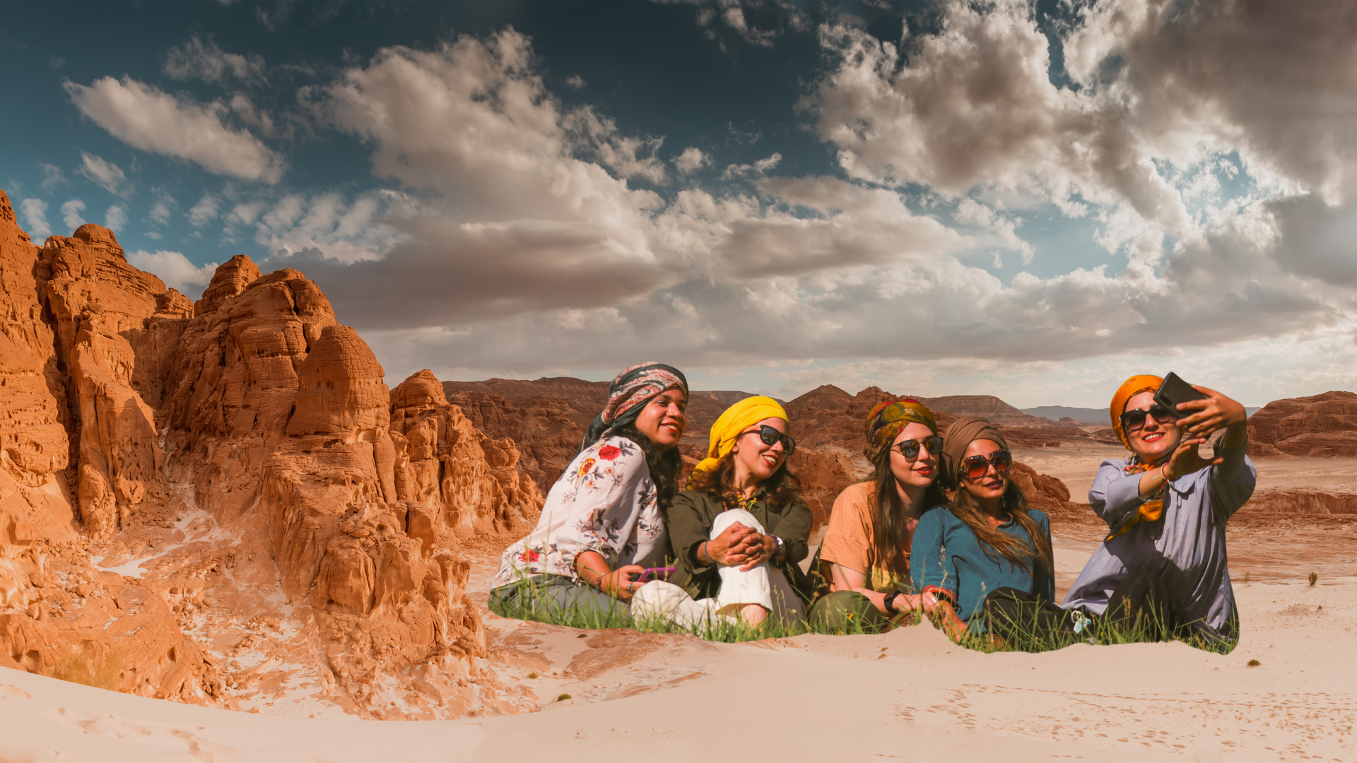 Five people wearing headscarves and sunglasses pose for a selfie in a desert landscape.