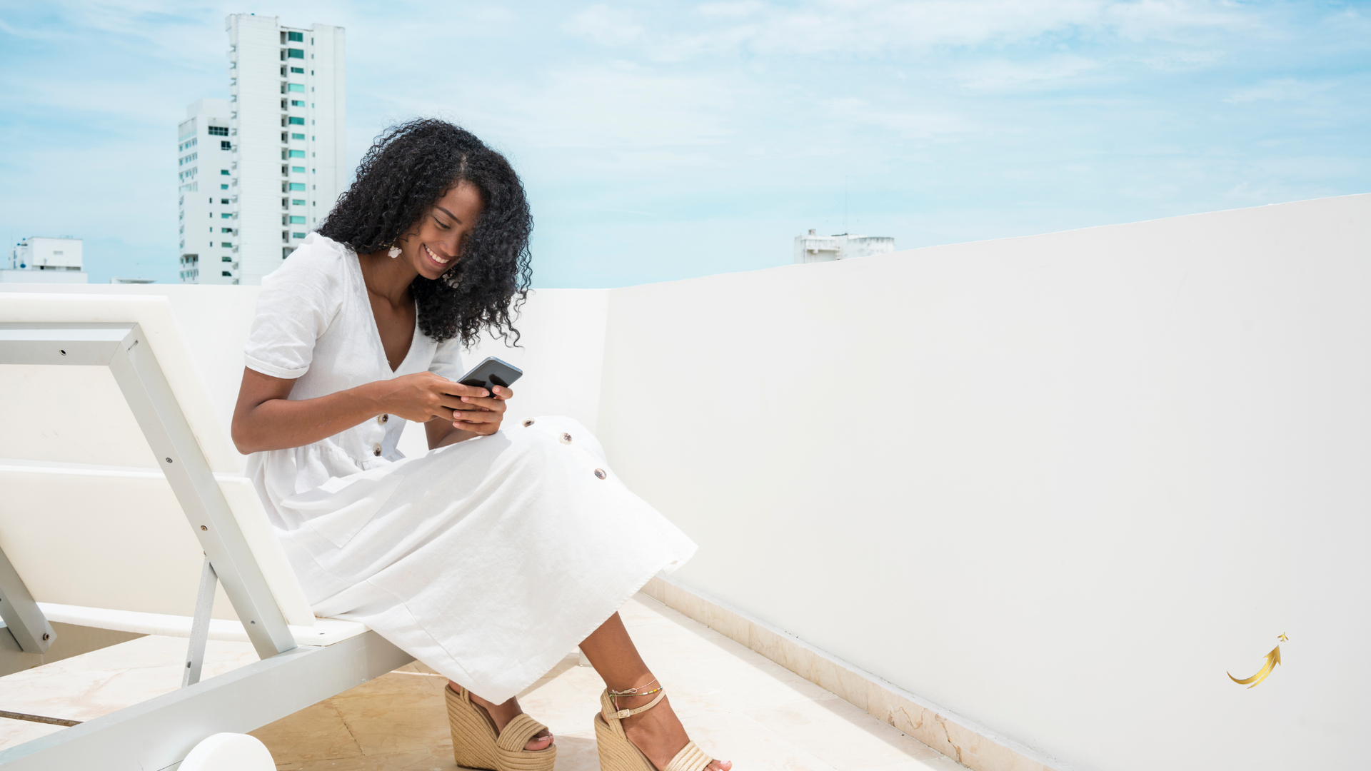 Woman in a white dress sitting on a rooftop, looking at her phone with city buildings in the background