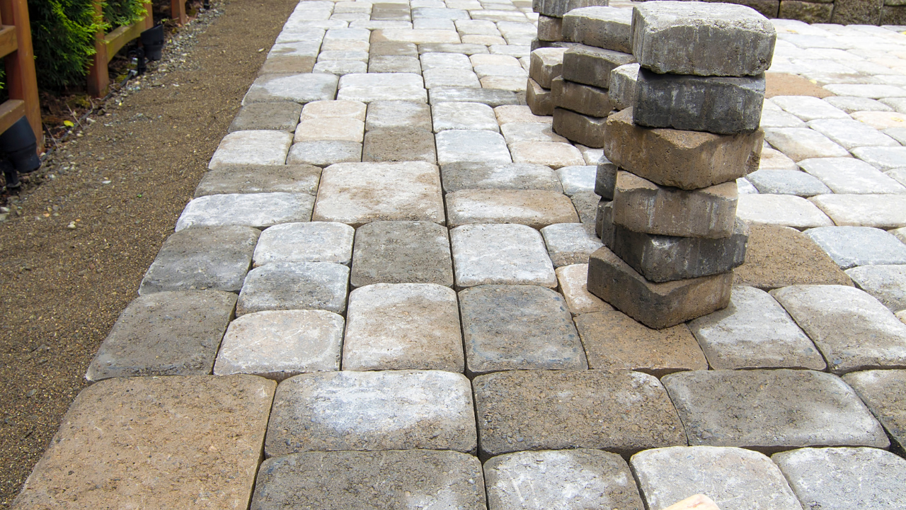 Stone pavers in various shades of gray and brown laid on a patio, with a stack of extra pavers on the side.