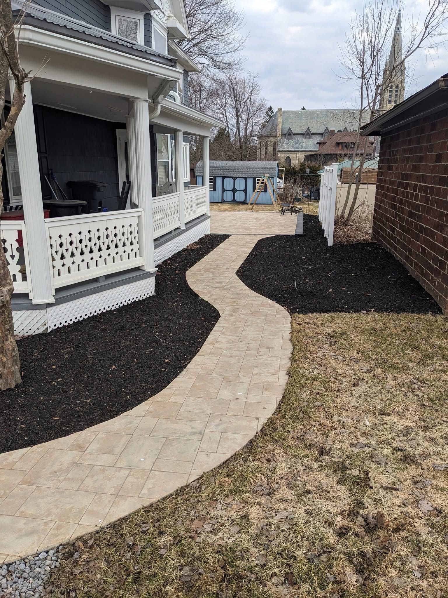 Beige stone path winds past a house with white porch and black mulch.