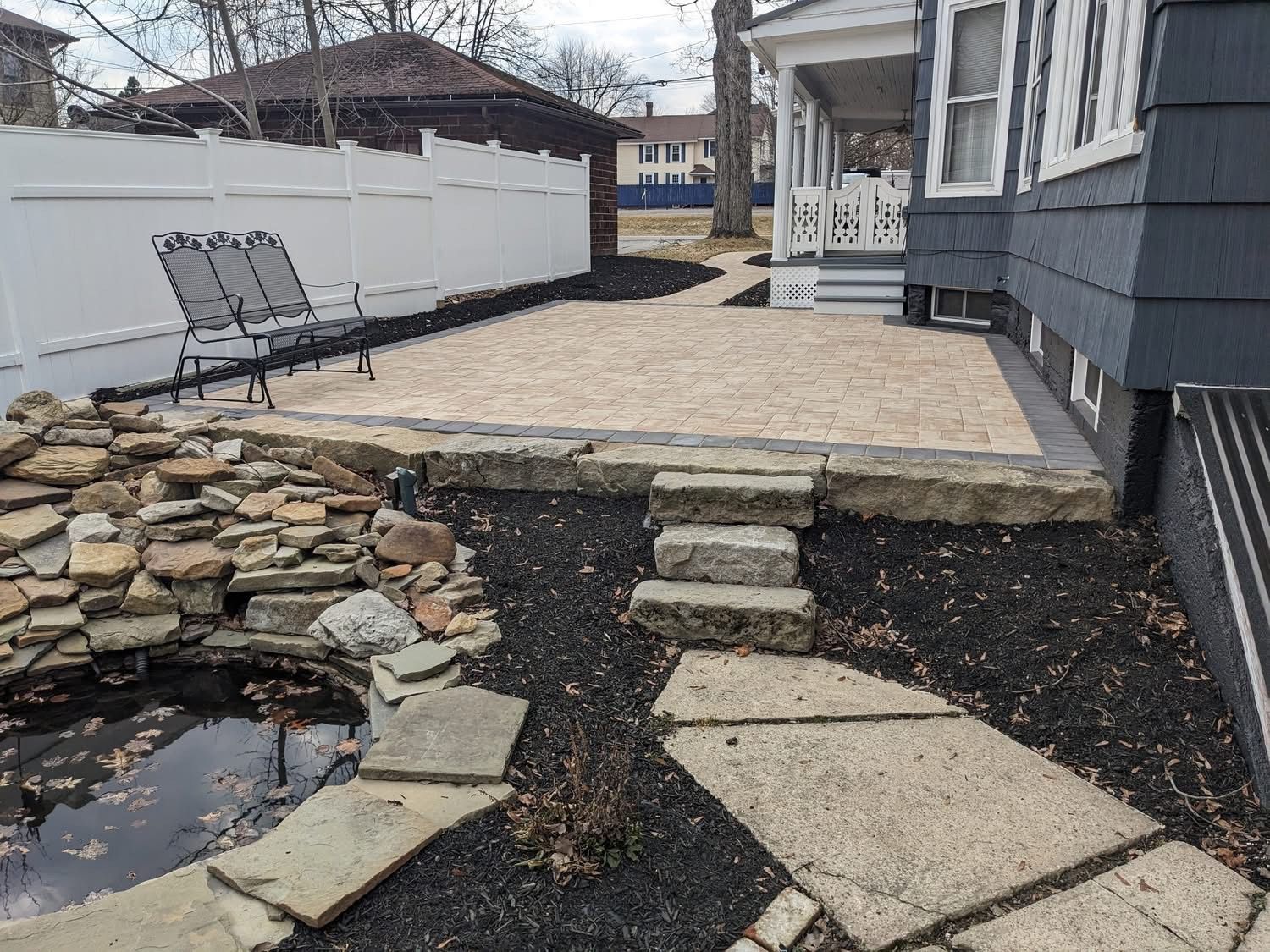 Backyard patio with gravel, bench, pond, stone steps, and dark mulch.