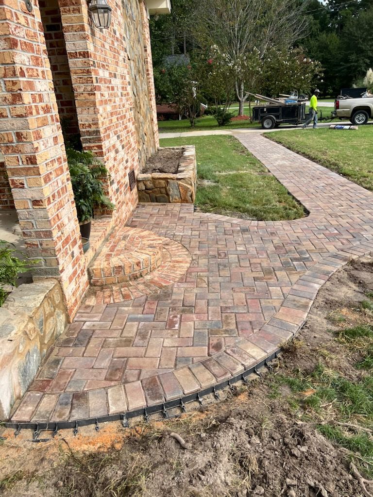 Brick pathway leading to a house entrance with brick columns. Green lawn and a parked truck are in the background.