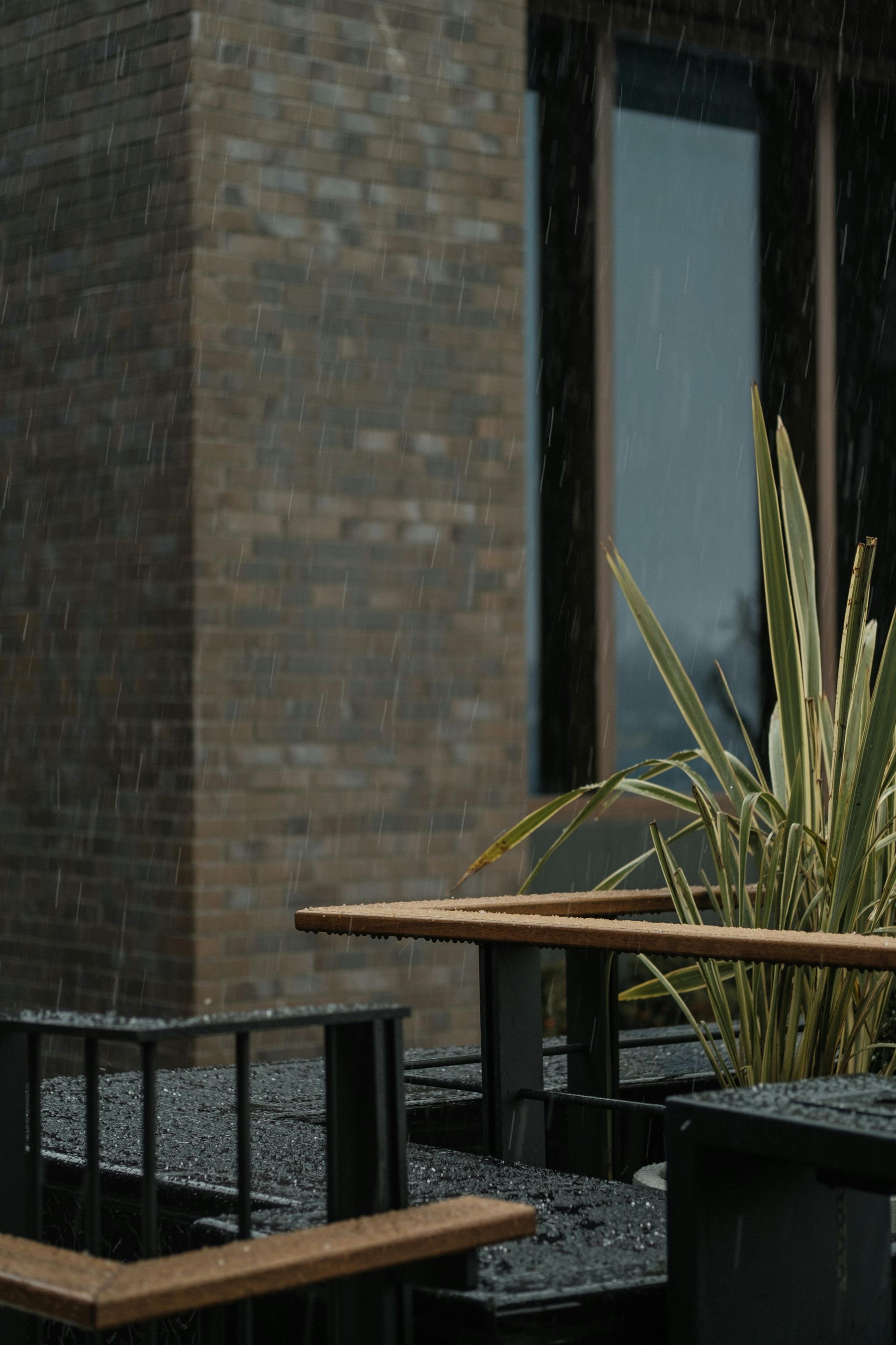 Rain falling on outdoor seating area near a brick building.