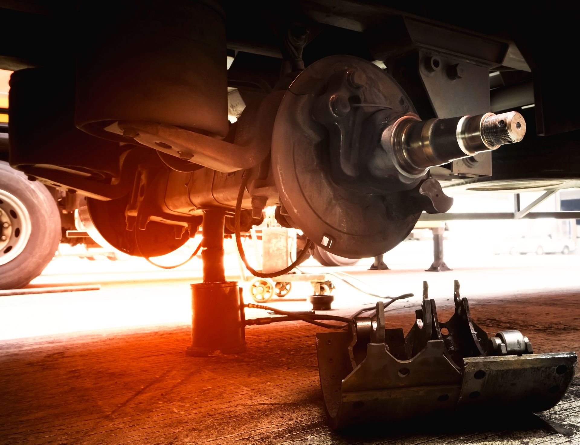 Car lifted on jack with exposed wheel hub in a garage, warm light shining underneath