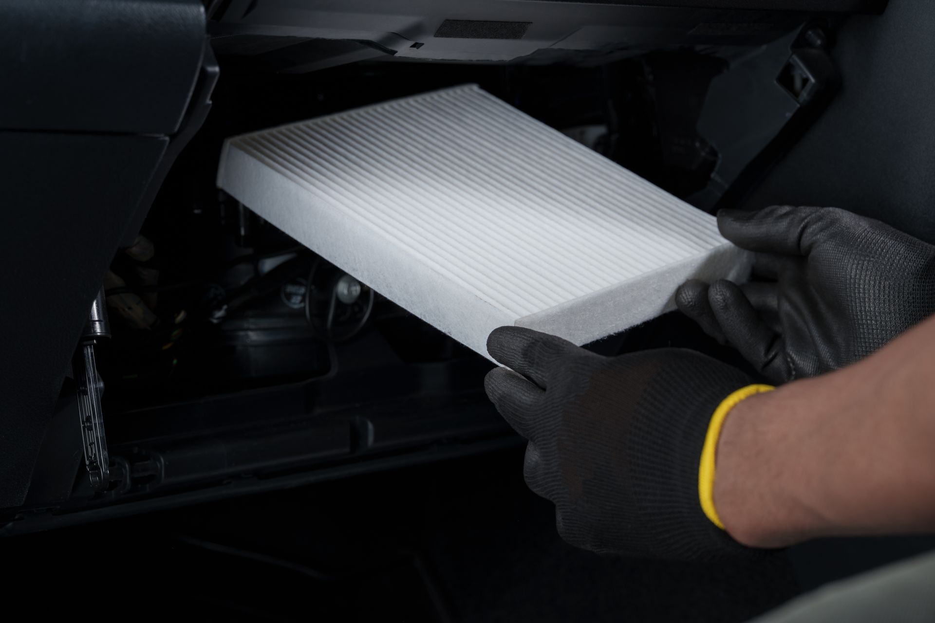 Gloved hands inserting a white cabin air filter into a car dashboard slot