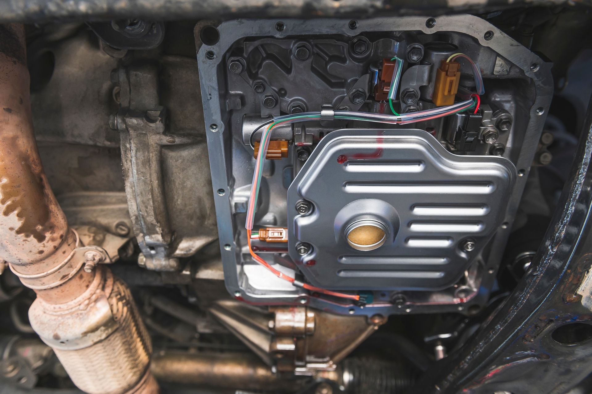 Undercarriage view of a vehicle with a black and silver transmission pan and exposed wiring.