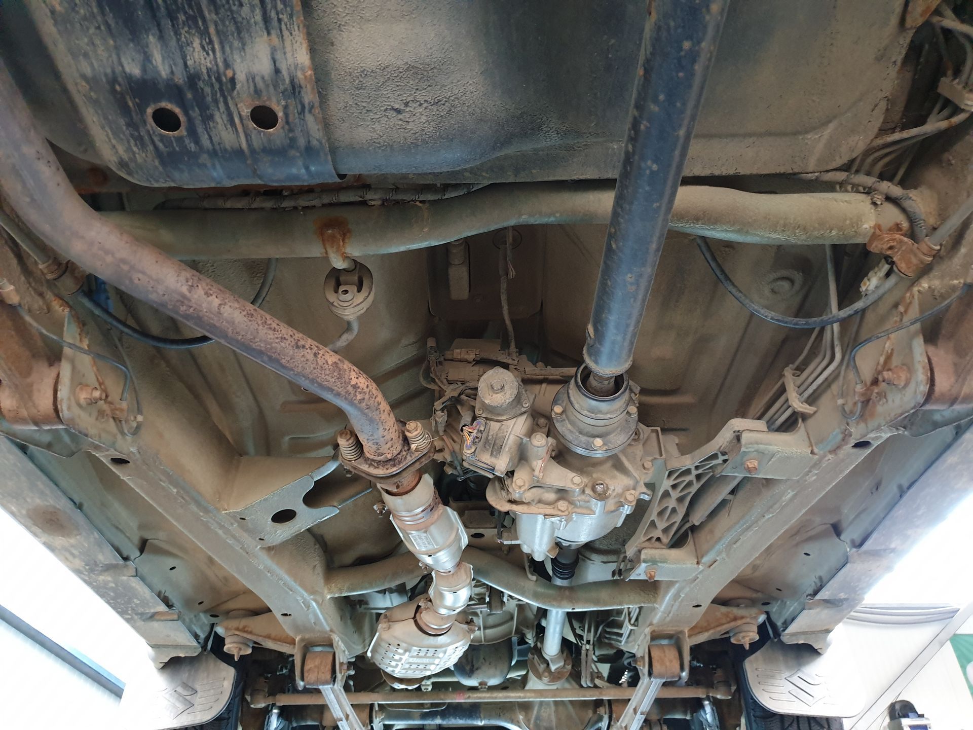 Undercarriage of a vehicle showing exhaust and drivetrain components, with rust and grime visible.