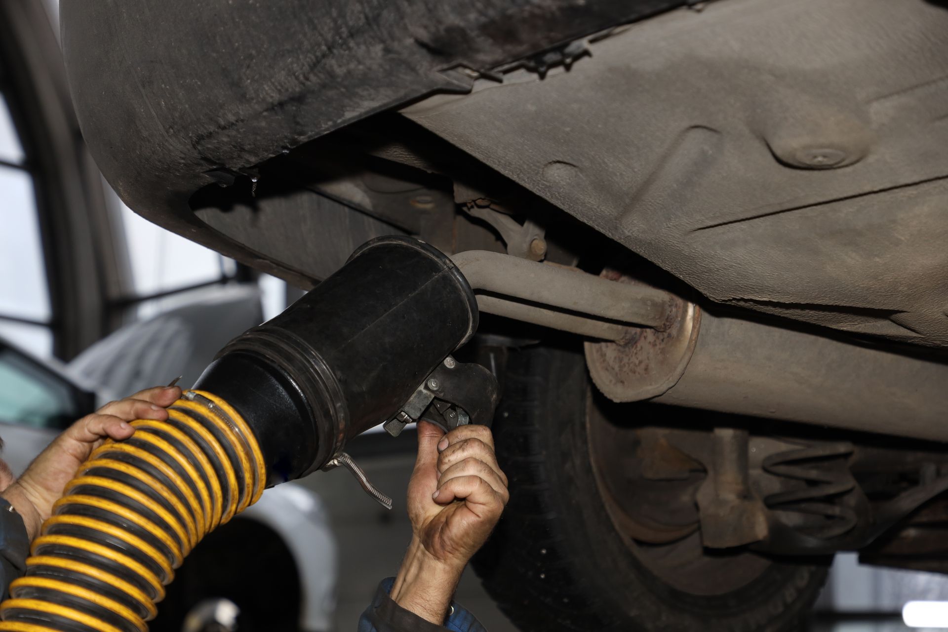 Mechanic using a hose to vacuum debris from under a car seat