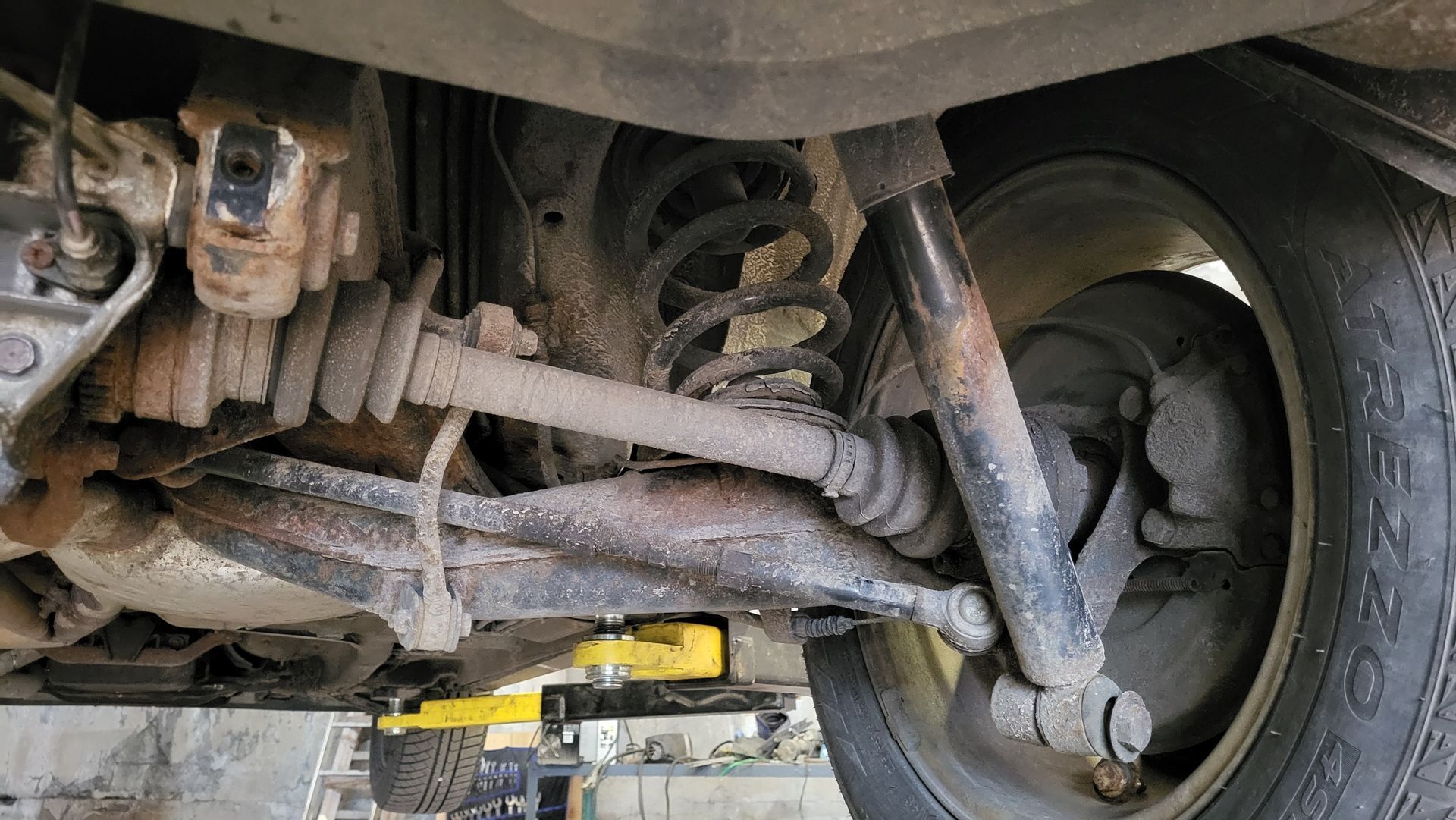 Undercarriage of a vehicle showing suspension, axle, and a rear tire in a garage