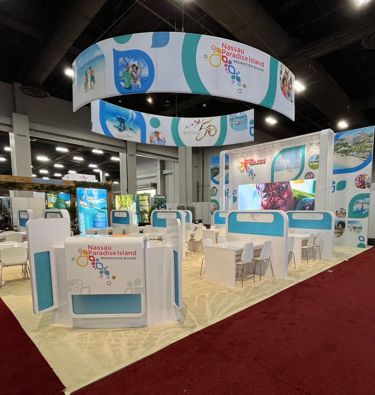 Bright blue-and-white trade show booth with hanging banners, display counters, and chairs on an expo floor