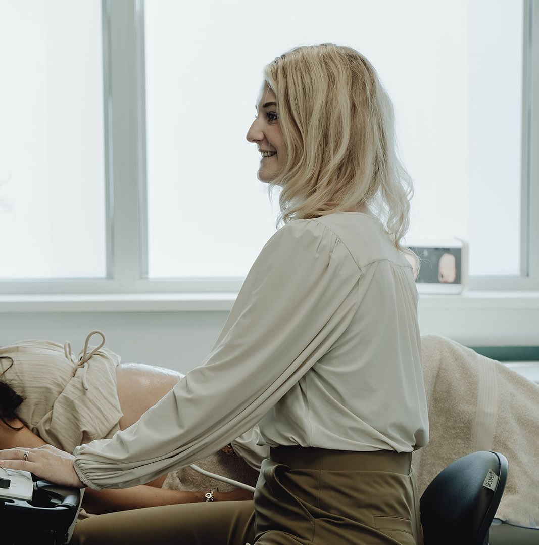 Een vrouw met blond haar lacht terwijl ze een patiënt behandelt in een goed verlichte kamer.