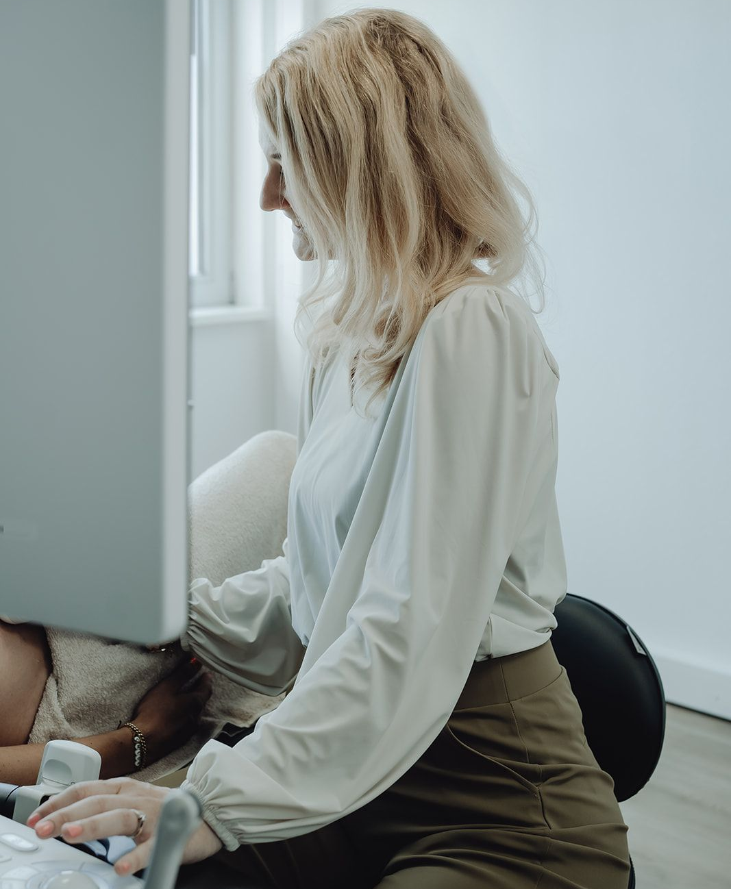 Een vrouw voert binnenshuis een echo uit bij een patiënt. De vrouw is blond en draagt een witte blouse.