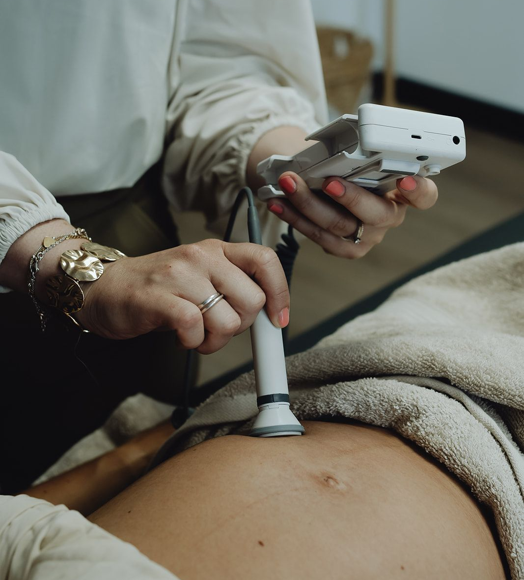 Persoon die een draagbaar echografie-apparaat op een zwangere buik gebruikt.