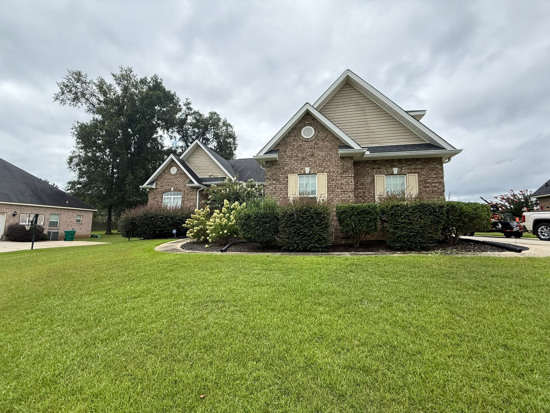 Brick house with green lawn and landscaping under a cloudy sky.