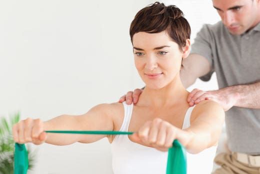 Woman doing arm exercise with resistance band, with therapist's support.