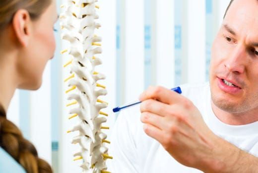 A healthcare provider points to a spinal model, explaining it to a patient in an office.