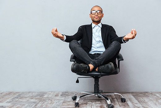 Man in office attire meditating in an office chair, with hands in a mudra position.