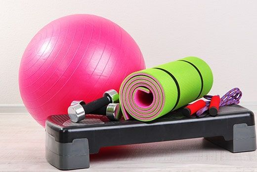 Pink exercise ball, green mat, dumbbells, step platform, resistance bands. Fitness equipment on white background.
