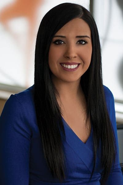 Woman with long black hair, smiling, wearing a blue dress.