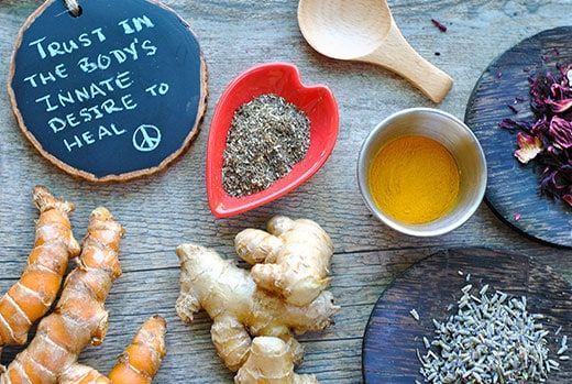 Various herbs and spices on a wooden table, including turmeric, ginger, and a sign that says,