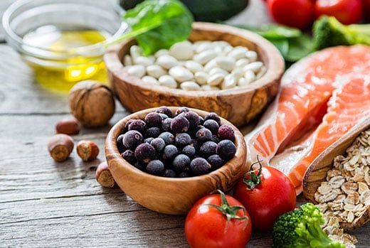Assortment of healthy foods, including fish, beans, berries, nuts, vegetables, and olive oil, on a wooden surface.