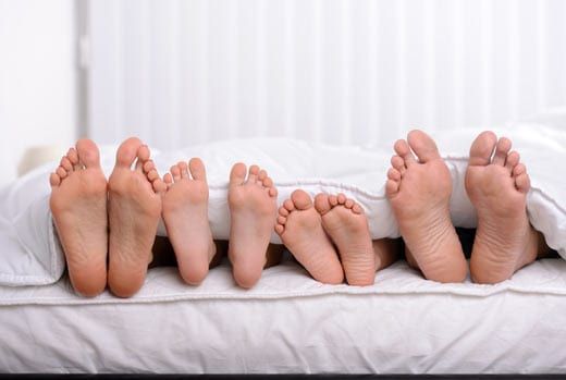 Six bare feet sticking out from under white bedding.