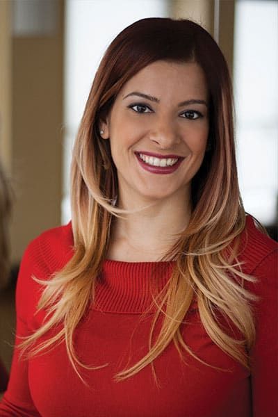 Woman with ombre hair smiles, wearing a red sweater.
