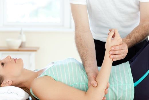 Woman receiving arm therapy from a person in a medical setting.