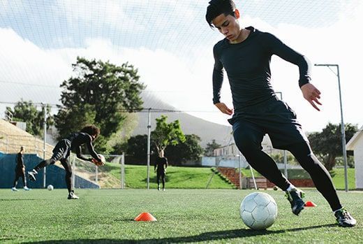 Soccer player dribbles ball on a green field during practice.
