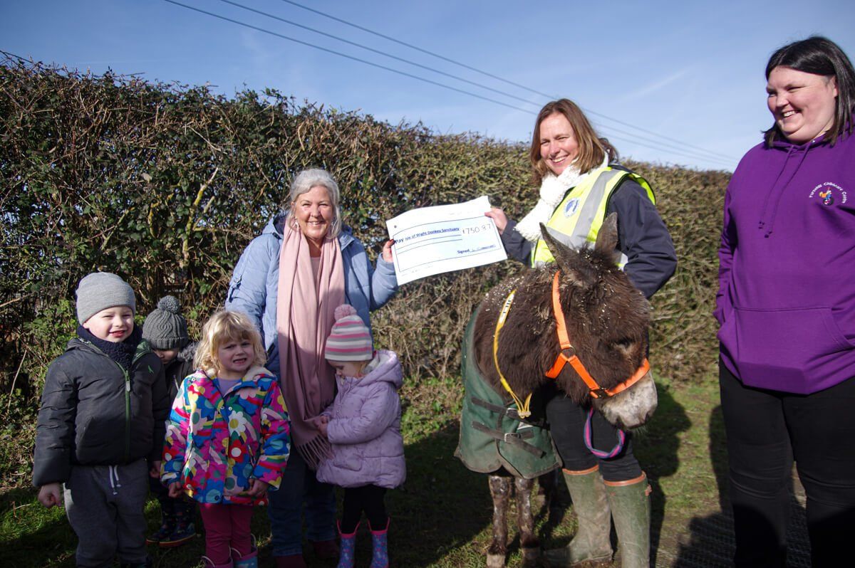 Group of people and children presenting a cheque with a donkey at the Isle of Wight Donkey Sanctuary