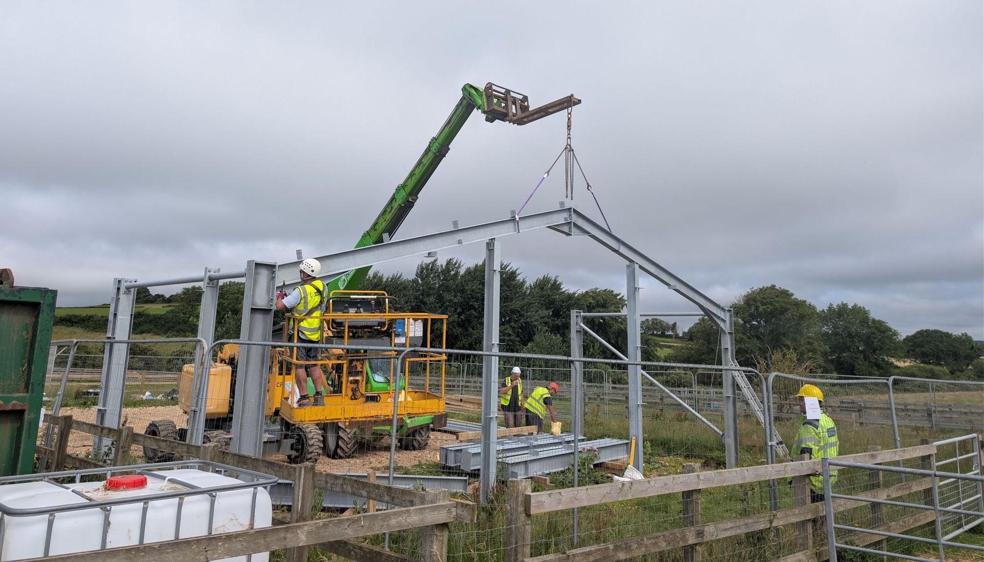 A crane lifting steelwork into place. People in hi vis jackets and wearing hard hats are on the ground. 