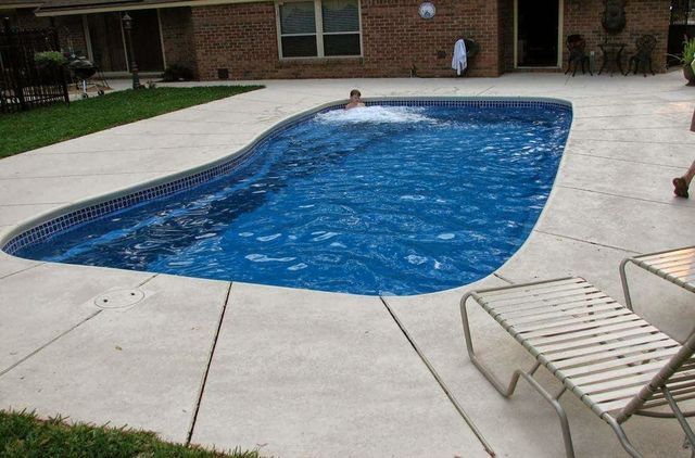 Backyard swimming pool covered with blue tarp, surrounded by concrete patio and lounge chair.