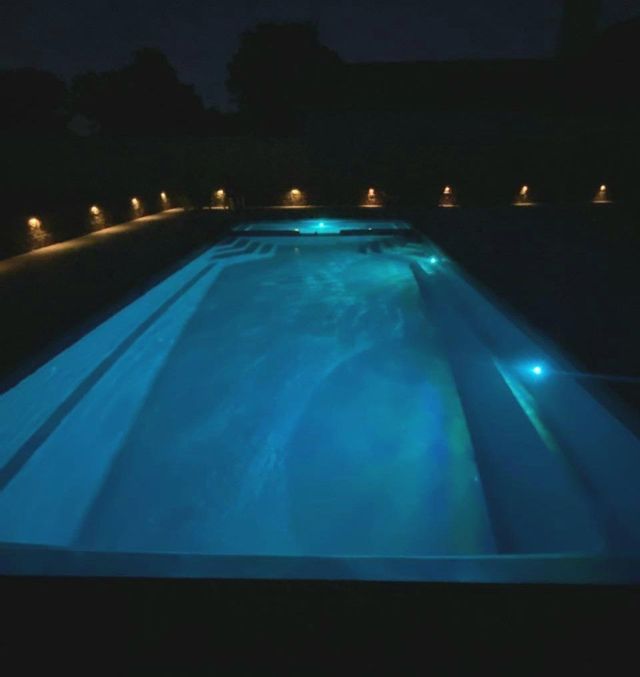 Illuminated backyard swimming pool at night with blue water and small garden lights along the edge