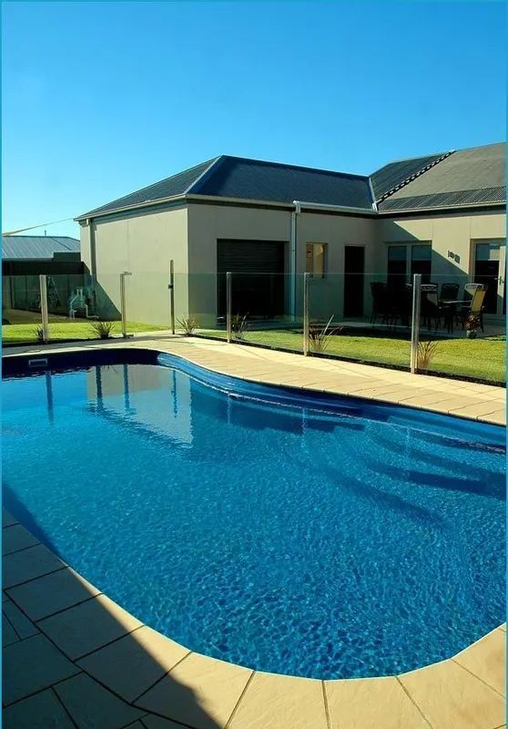 Backyard swimming pool with blue water, concrete deck, and trees beside a house