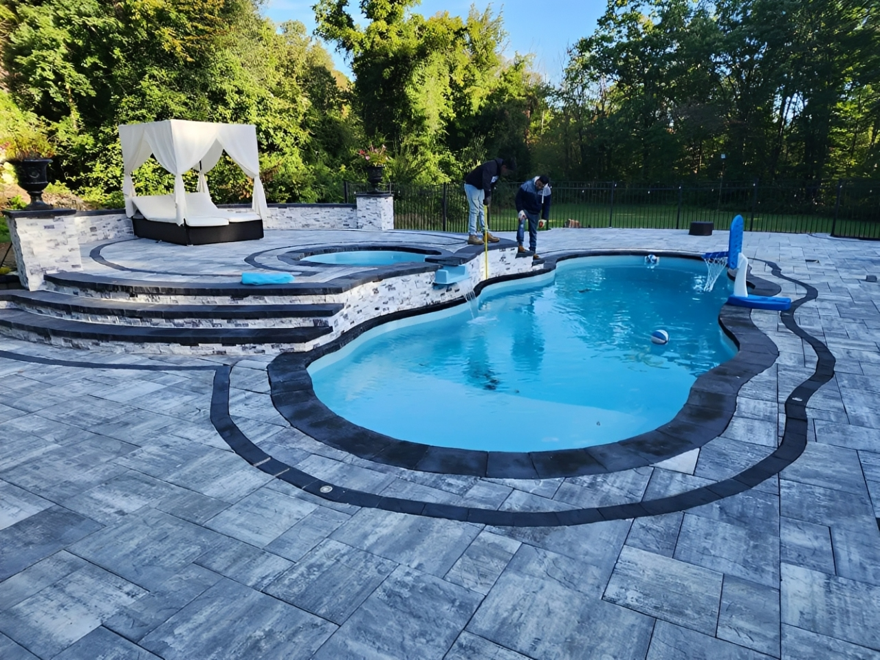 Backyard swimming pool with blue water, concrete deck, and trees beside a house