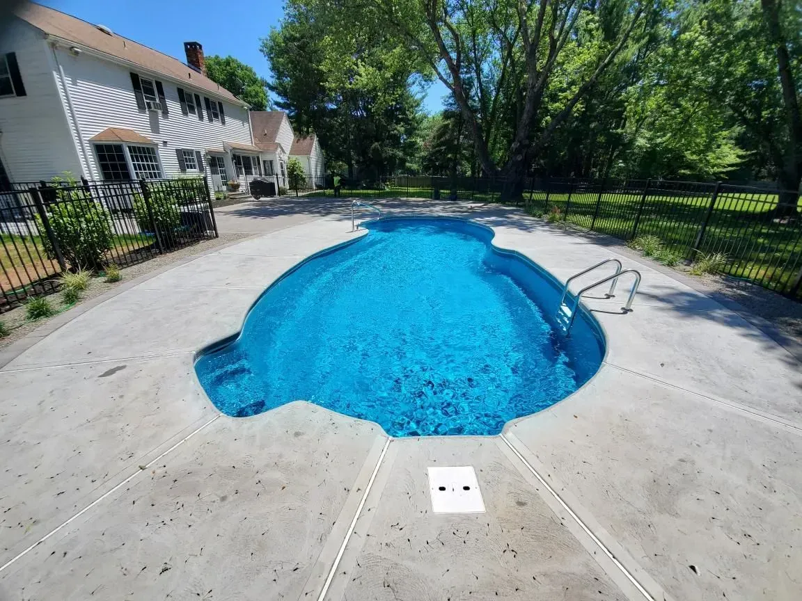 Backyard swimming pool with blue water, concrete deck, and trees beside a house