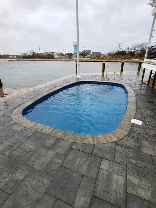 Small blue pool on a waterfront deck with gray pavers and a cloudy sky