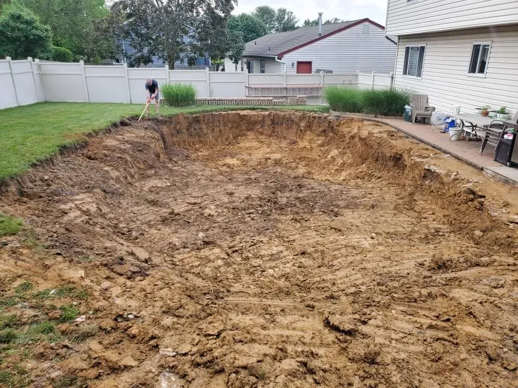 Backyard with large excavated dirt area beside a house, fence, and lawn