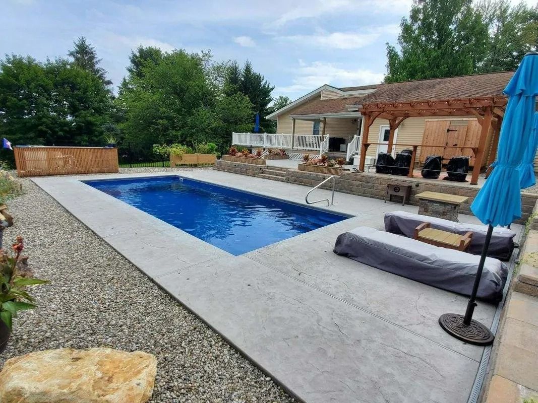 Backyard pool with blue water, lounge chairs, umbrella, and patio seating beside a house