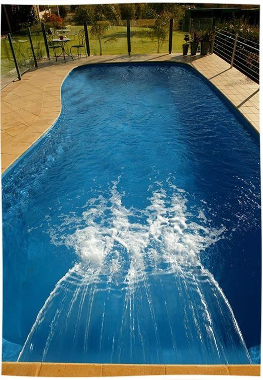 Blue swimming pool with a splash in the center, surrounded by a tan deck and black railings