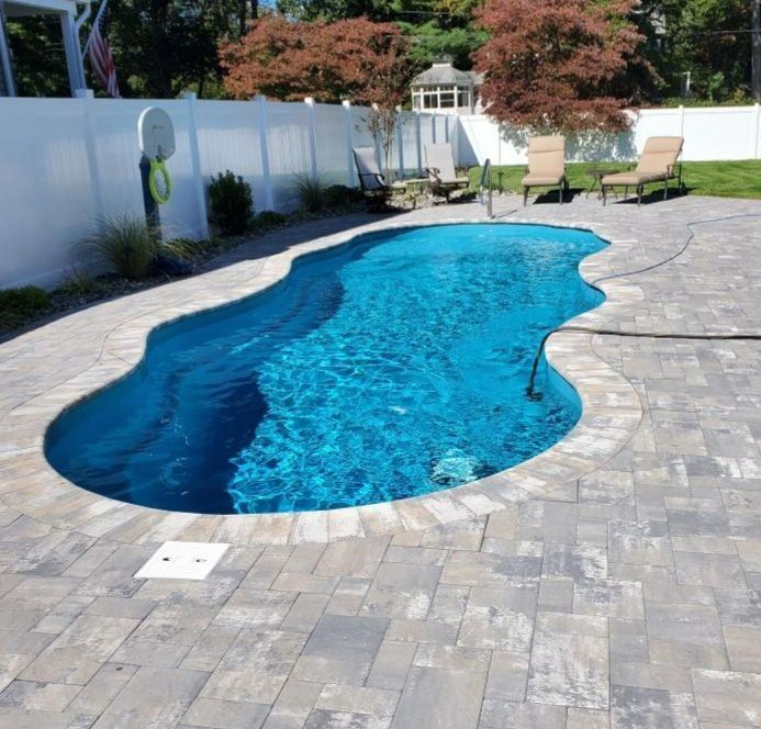 Backyard swimming pool with blue water, paver patio, lounge chairs, and white fence