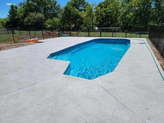 Backyard swimming pool with light blue water and a concrete deck, surrounded by a black fence and trees