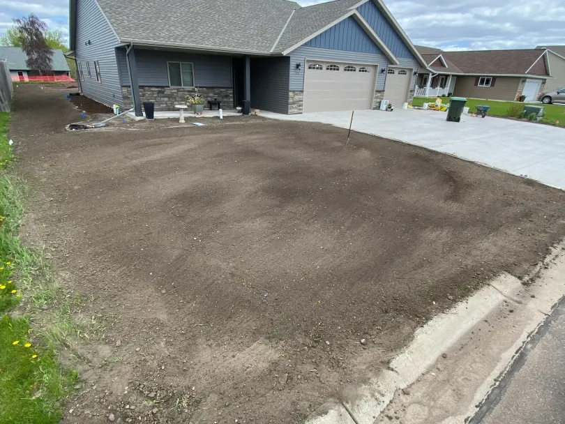 Freshly seeded front yard with a suburban house, driveway, and sidewalk along the street