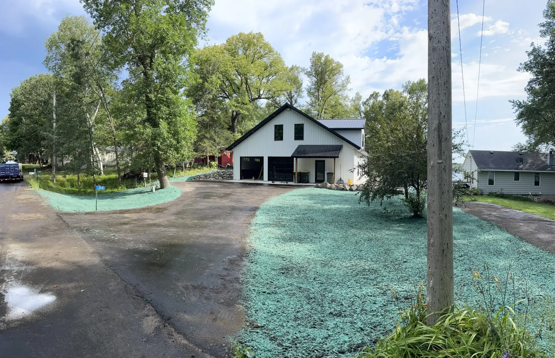 Driveway leading to a white house with trees and a utility pole in a wooded yard.