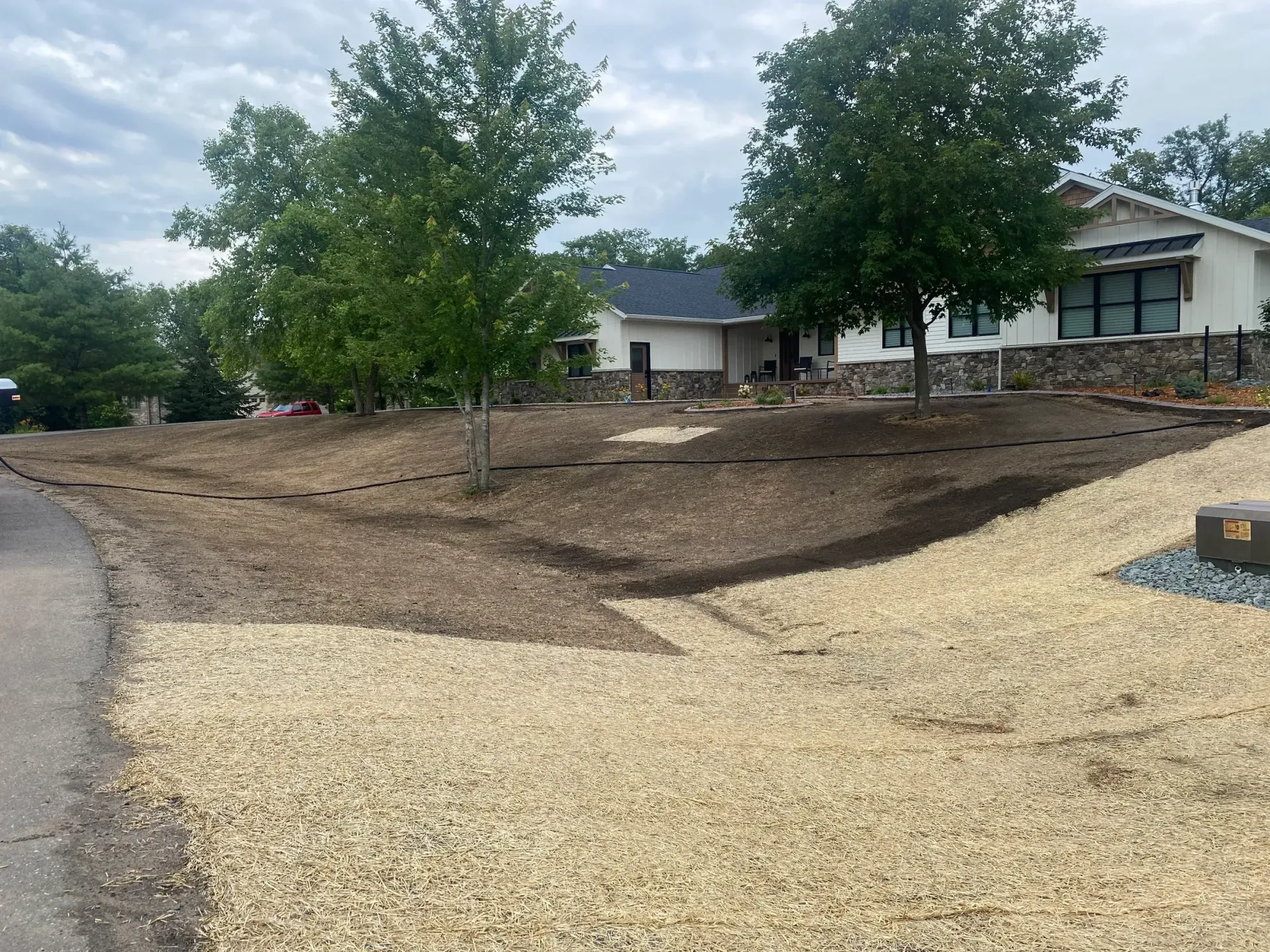 Gravel path and dirt landscaping with young trees beside a suburban house under cloudy skies