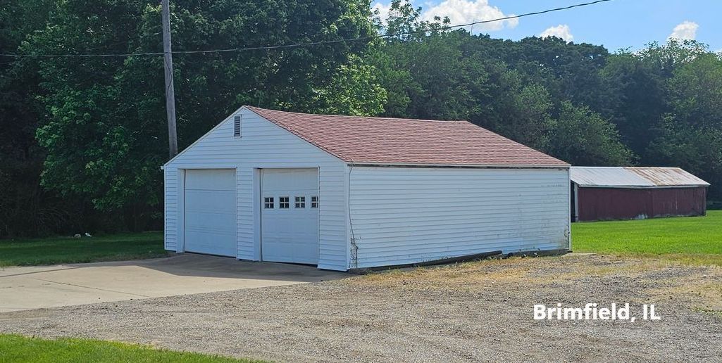 A white garage with a red roof is sitting in the middle of a grassy field.